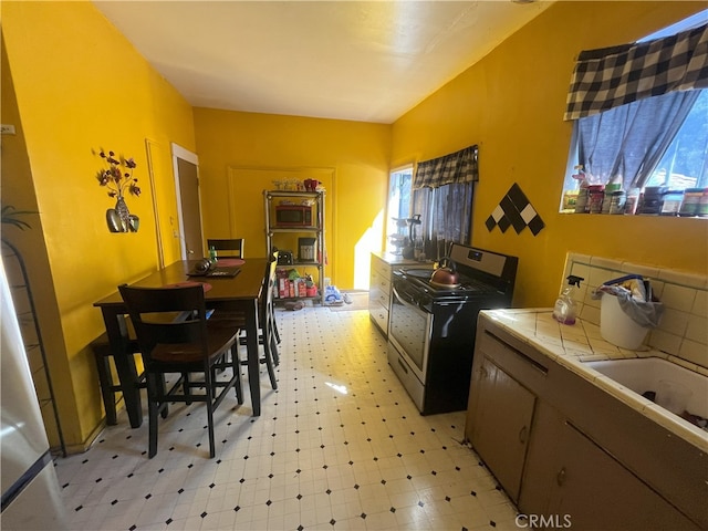 kitchen featuring decorative backsplash, tile countertops, light floors, and stainless steel range with electric cooktop