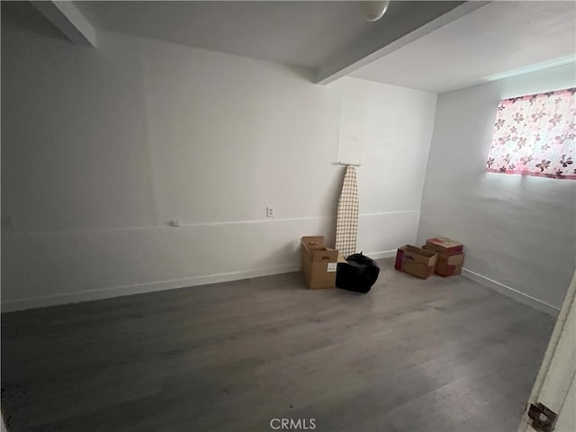 unfurnished room featuring beam ceiling, wood finished floors, and baseboards