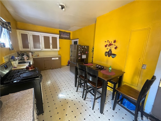 kitchen featuring light floors, light countertops, glass insert cabinets, gas range, and stainless steel fridge