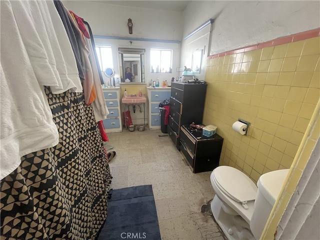 bathroom with a wainscoted wall, toilet, vanity, tile patterned floors, and tile walls