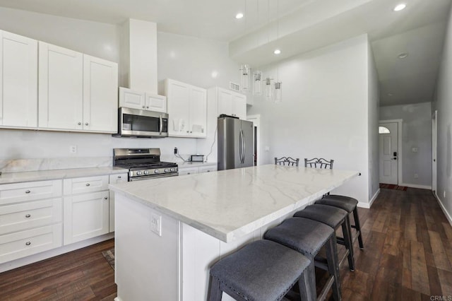 kitchen with a kitchen island, a breakfast bar, stainless steel appliances, dark wood-type flooring, and white cabinetry