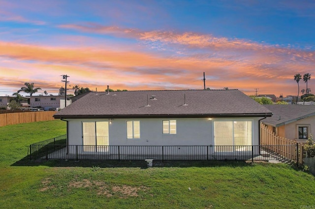 back of house featuring stucco siding, a lawn, roof with shingles, and fence