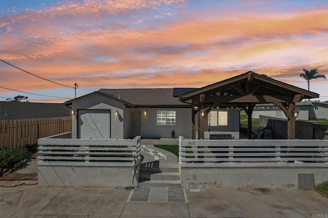 view of front facade with stucco siding, a fenced front yard, a gazebo, an attached garage, and solar panels