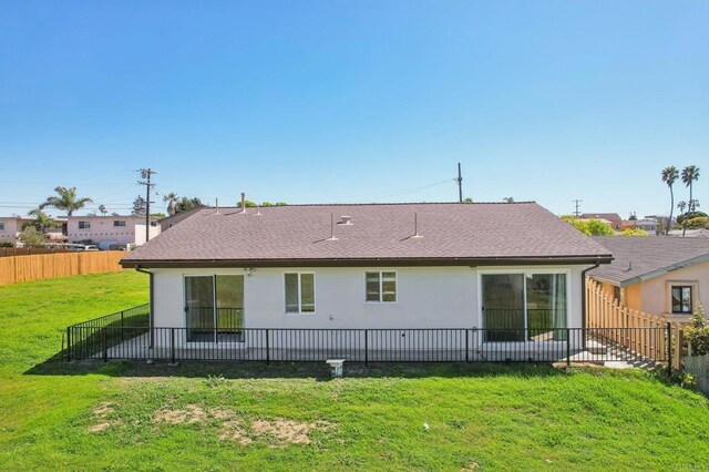 rear view of property featuring stucco siding, a lawn, roof with shingles, and fence