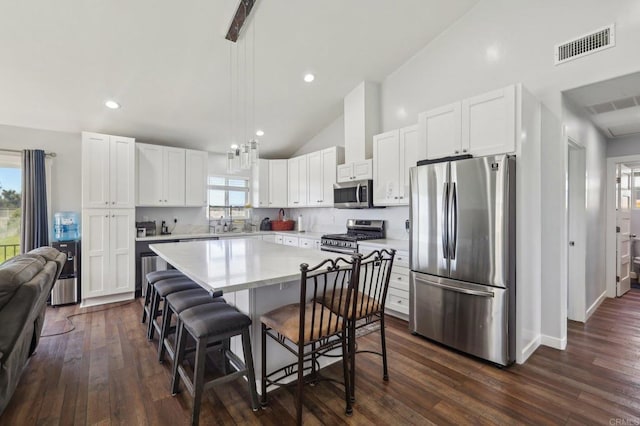 kitchen featuring visible vents, a kitchen island, a breakfast bar, light countertops, and stainless steel appliances