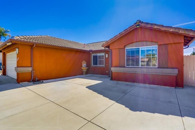 exterior space featuring stucco siding, fence, concrete driveway, a garage, and a tiled roof