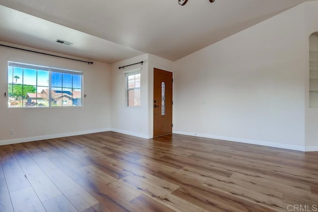 unfurnished room featuring arched walkways, visible vents, baseboards, and wood finished floors