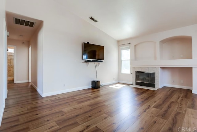 unfurnished living room featuring vaulted ceiling, visible vents, a tiled fireplace, and wood finished floors