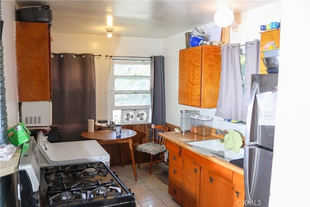 kitchen featuring a sink, freestanding refrigerator, brown cabinetry, light countertops, and light tile patterned floors