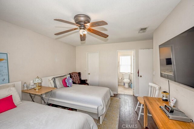 bedroom with a ceiling fan, ensuite bath, wood finished floors, and visible vents