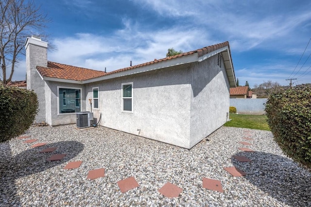 back of property featuring stucco siding, a tile roof, fence, central AC unit, and a chimney