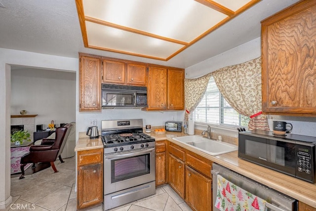 kitchen with light countertops, brown cabinets, appliances with stainless steel finishes, a fireplace, and a sink