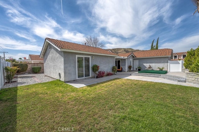 rear view of house with stucco siding, a lawn, fence private yard, and a tile roof