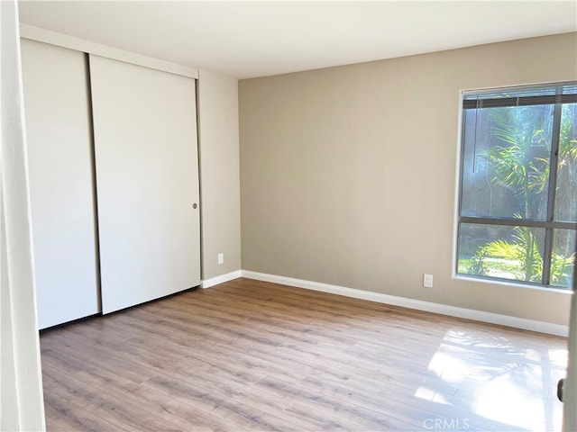 unfurnished bedroom featuring baseboards, multiple windows, a closet, and wood finished floors