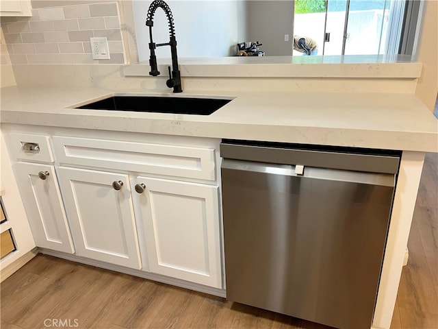 kitchen with a sink, tasteful backsplash, stainless steel dishwasher, light wood-style floors, and white cabinets