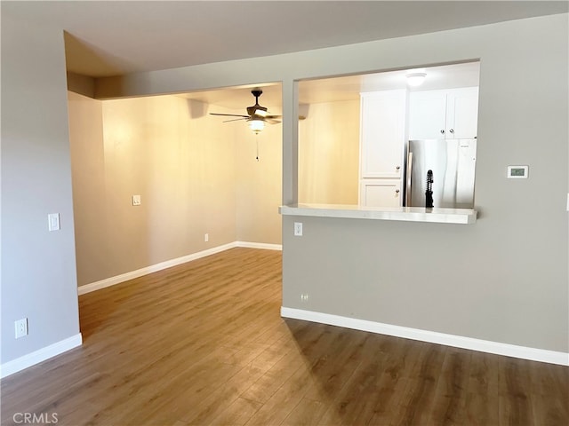 unfurnished living room featuring a ceiling fan, wood finished floors, and baseboards