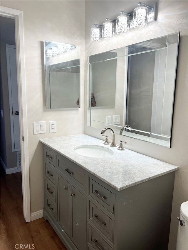 bathroom featuring visible vents, baseboards, toilet, wood finished floors, and vanity