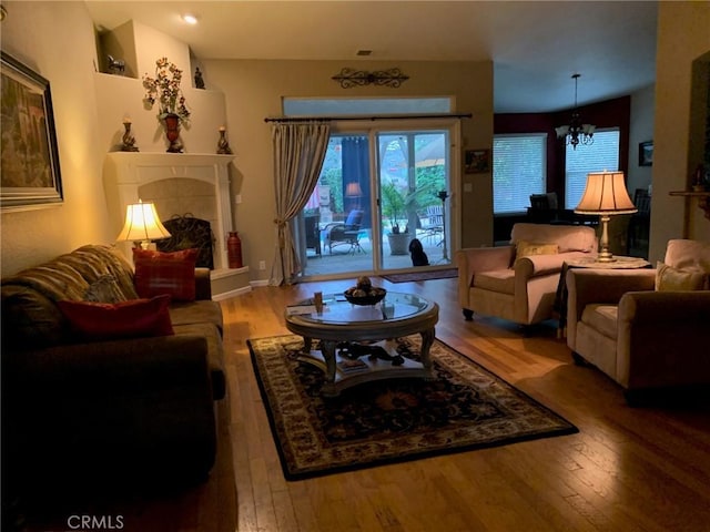 living area featuring an inviting chandelier, wood-type flooring, and a tile fireplace