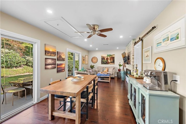 dining space with dark wood finished floors, a barn door, attic access, and a ceiling fan