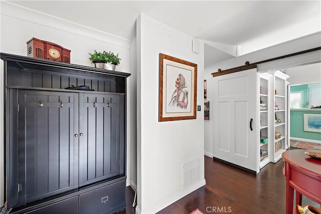 hallway featuring a barn door, dark wood-style floors, and visible vents