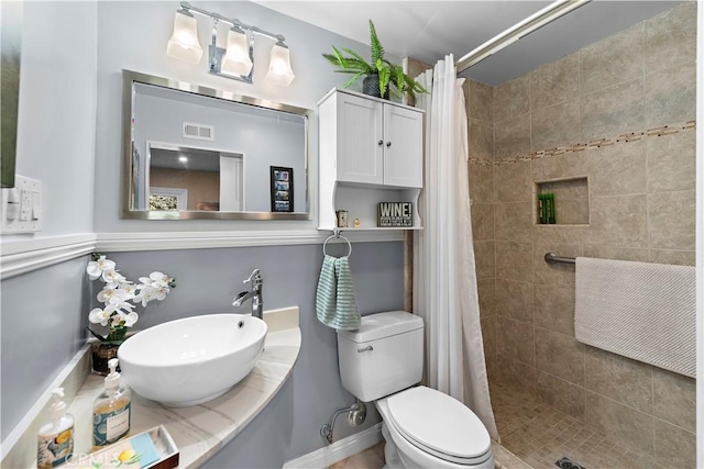 full bath with a sink, visible vents, toilet, and a tile shower