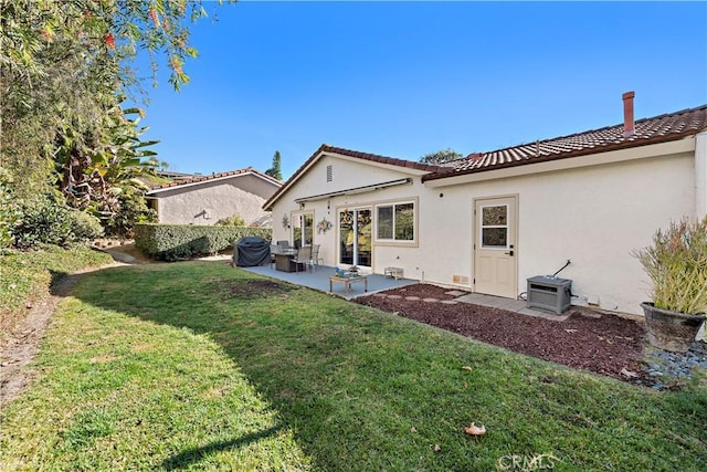 rear view of house featuring a patio, a tiled roof, a lawn, and stucco siding