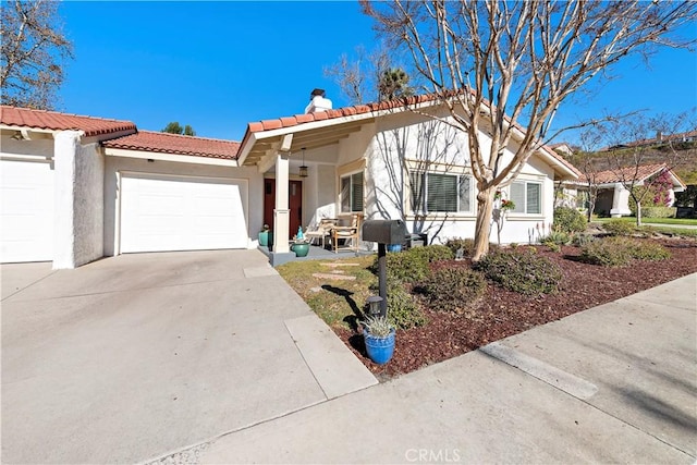 view of front of house with a tile roof, concrete driveway, stucco siding, a chimney, and an attached garage