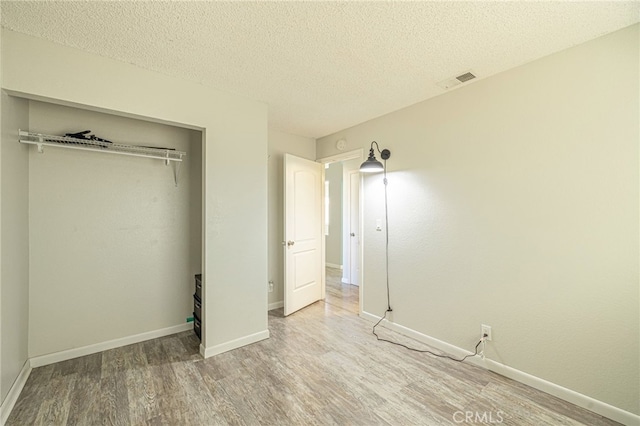 unfurnished bedroom with a closet, a textured ceiling, baseboards, and wood finished floors