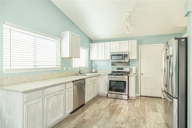 kitchen with vaulted ceiling, appliances with stainless steel finishes, light wood-style floors, a textured ceiling, and a sink