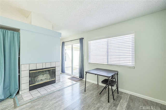 office area featuring baseboards, a textured ceiling, wood finished floors, and a tile fireplace