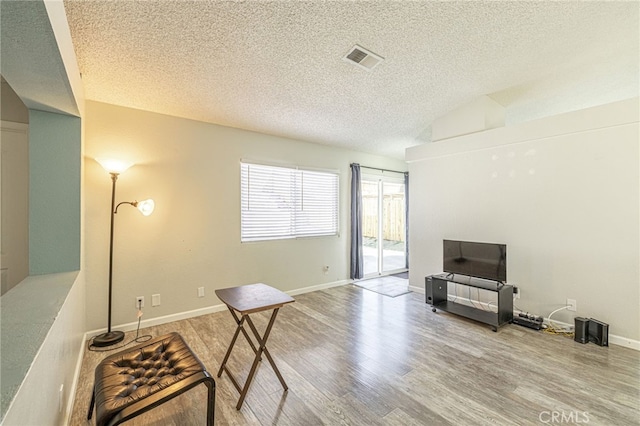 interior space with visible vents, a textured ceiling, baseboards, and wood finished floors