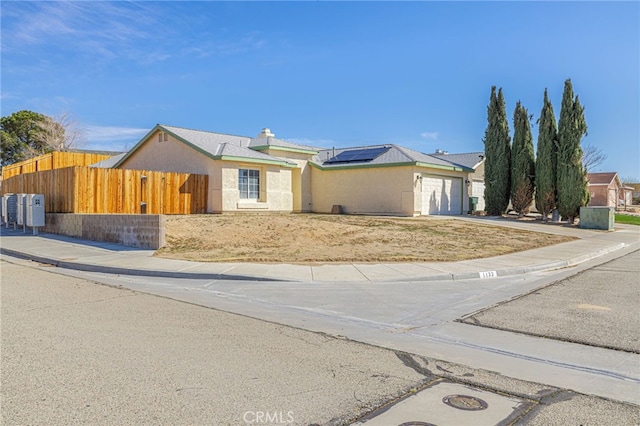 view of front of home with stucco siding, fence, concrete driveway, a garage, and solar panels