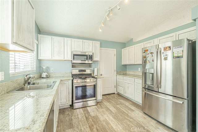 kitchen featuring appliances with stainless steel finishes, a textured ceiling, light wood-style floors, and a sink