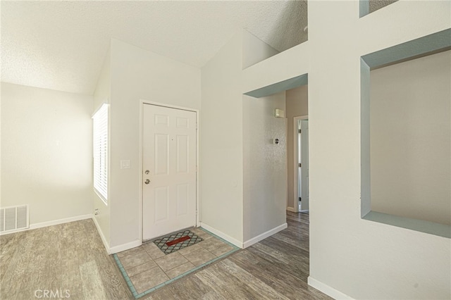 entrance foyer with visible vents, baseboards, vaulted ceiling, wood finished floors, and a textured ceiling