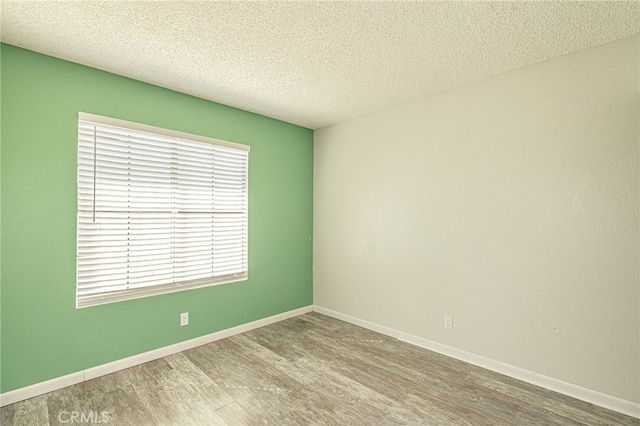 empty room with wood finished floors, baseboards, and a textured ceiling