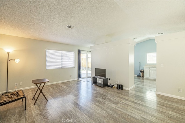 living area featuring visible vents, lofted ceiling, a textured ceiling, and wood finished floors