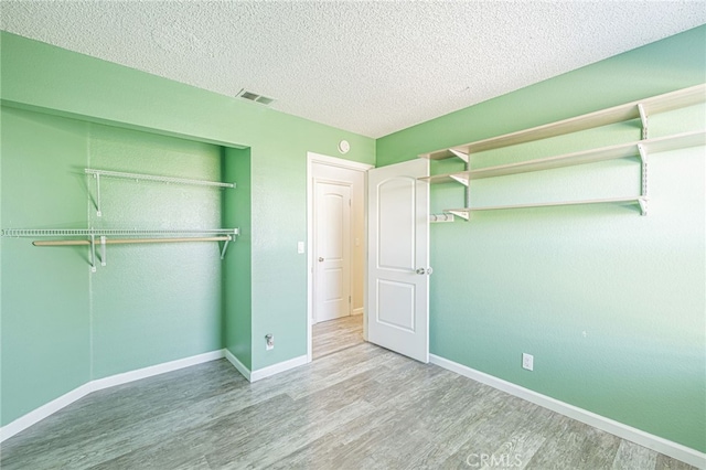 unfurnished bedroom with wood finished floors, visible vents, a closet, and a textured ceiling