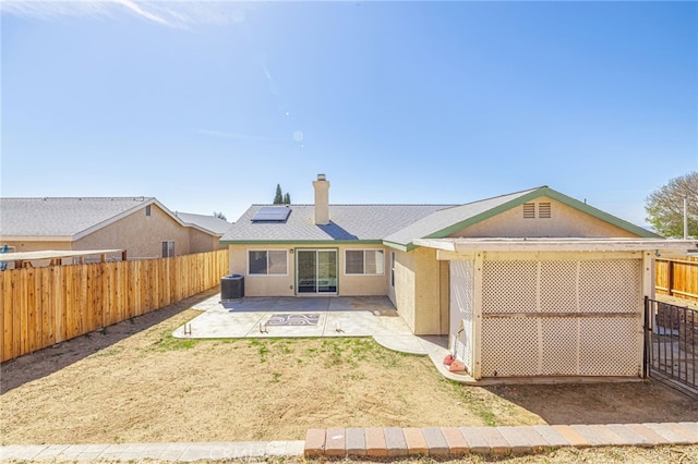 back of house featuring central AC, roof mounted solar panels, stucco siding, a fenced backyard, and a patio area