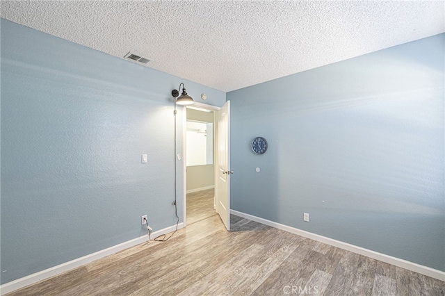 unfurnished room with a textured ceiling, wood finished floors, visible vents, and baseboards