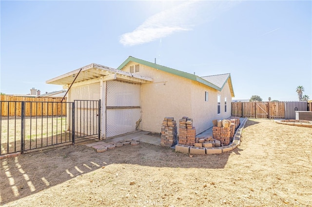 view of side of home featuring stucco siding, fence private yard, and a gate