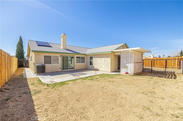 rear view of house featuring roof mounted solar panels, central AC unit, stucco siding, a fenced backyard, and a patio area