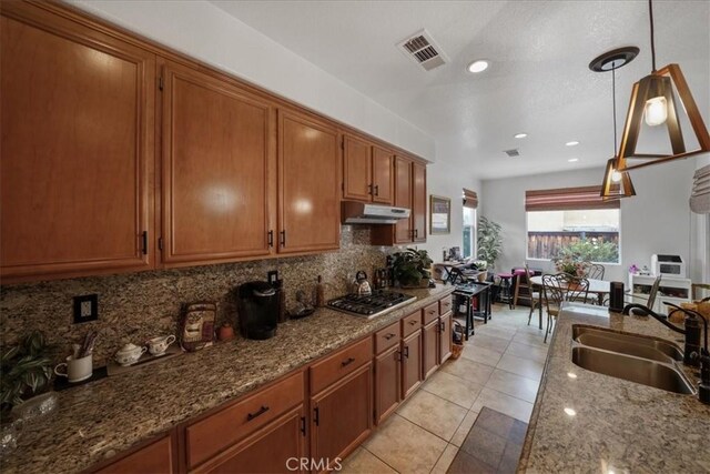 kitchen featuring visible vents, under cabinet range hood, decorative backsplash, brown cabinets, and a sink