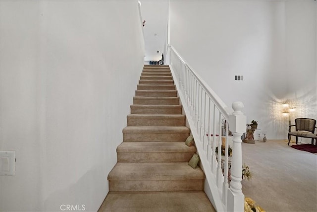 staircase featuring a high ceiling, visible vents, and carpet floors