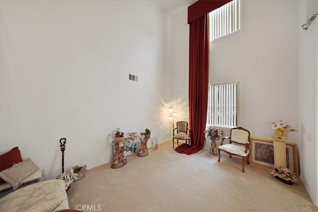 sitting room featuring visible vents, a high ceiling, and carpet