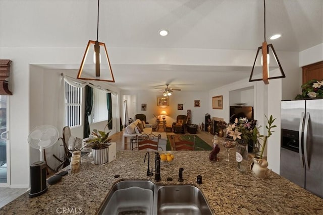 kitchen with open floor plan, stainless steel refrigerator with ice dispenser, stone countertops, a ceiling fan, and a sink