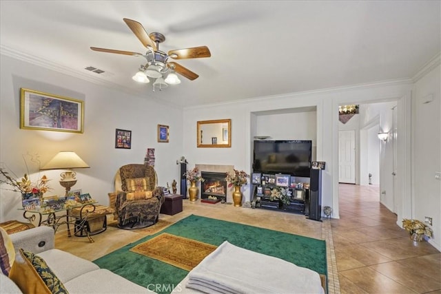 tiled living area with visible vents, crown molding, a ceiling fan, and a glass covered fireplace