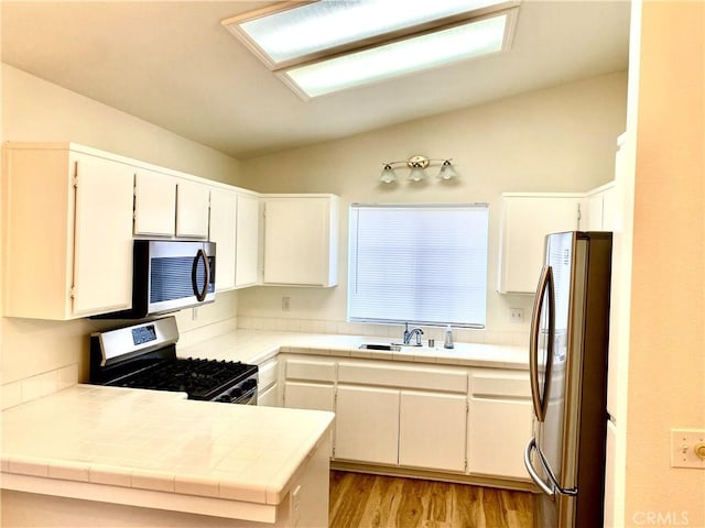 kitchen featuring a sink, white cabinetry, light wood-style floors, appliances with stainless steel finishes, and lofted ceiling