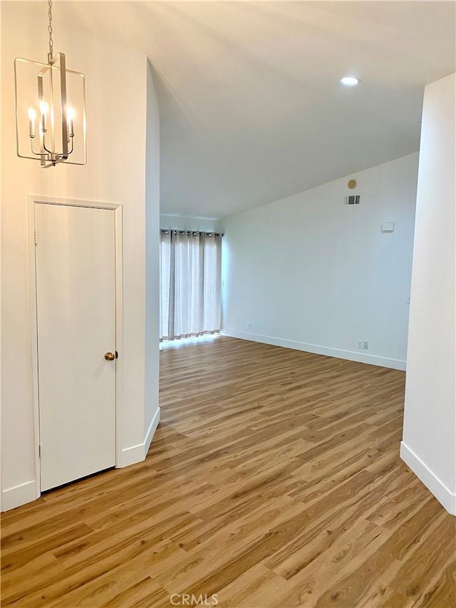 unfurnished room featuring visible vents, light wood-style flooring, baseboards, and an inviting chandelier