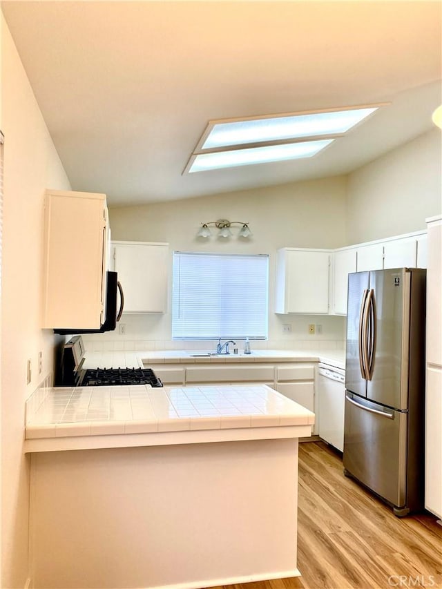 kitchen with a sink, freestanding refrigerator, range with gas cooktop, dishwasher, and tile counters