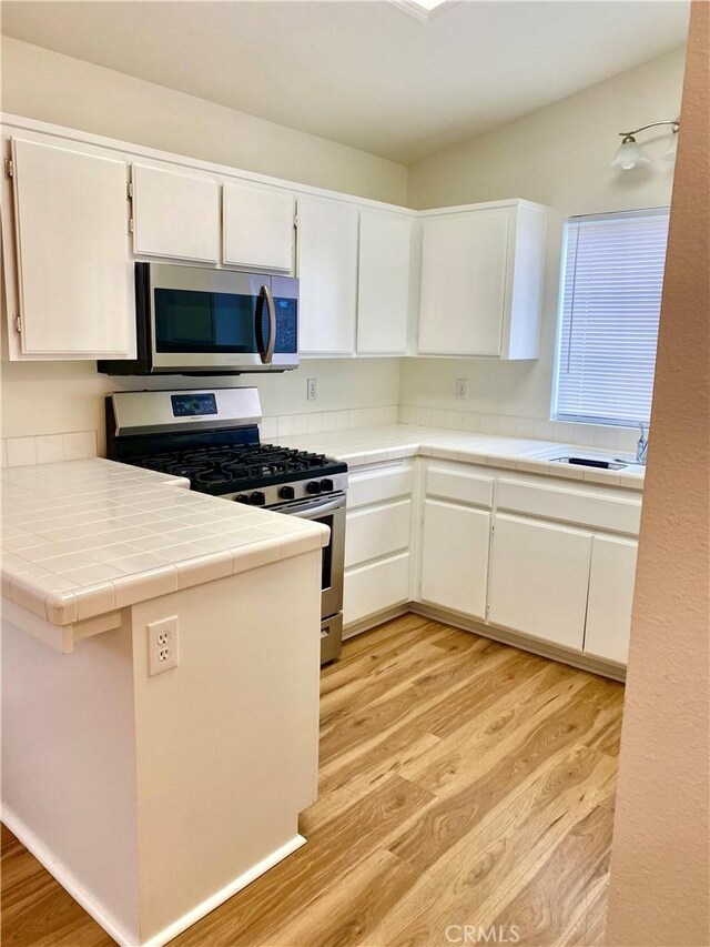 kitchen featuring tile counters, light wood-style flooring, white cabinets, and stainless steel appliances